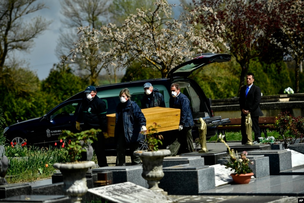 Personas con máscaras de protección para protegerse del coronavirus, cargan un ataúd en el cementerio Salvador, cerca de Vitoria,al norte de España. 