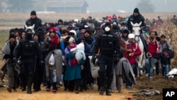Escorted by police, migrants move through fields after crossing from Croatia, in Rigonce, Slovenia, Oct. 27, 2015.