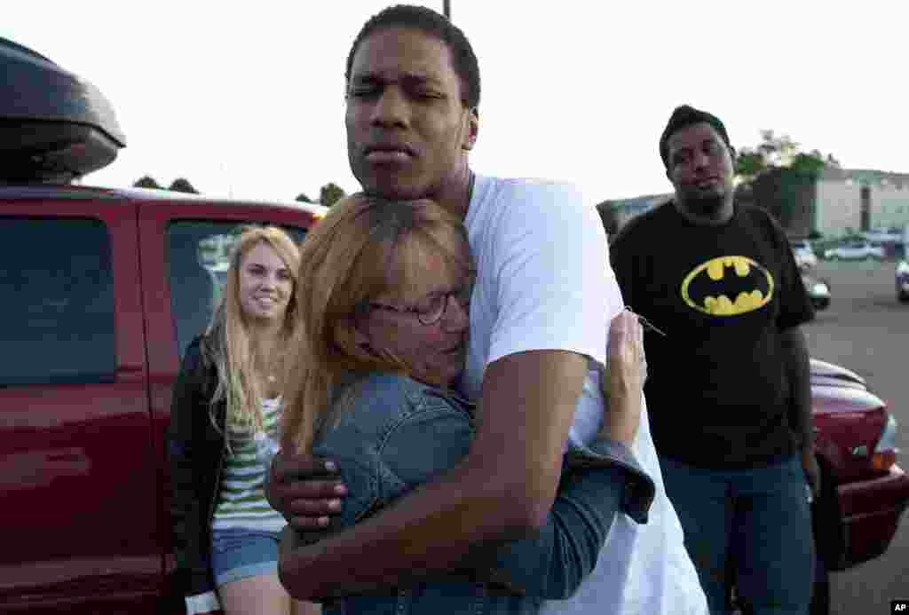 Judy Goos, second from left, hugs her daughter's friend, Isaiah Bow, 20, while eye witnesses Emma Goos, 19, left, and Terrell Wallin, 20, right, gather outside Gateway High School where witnesses were brought for questioning July 20, 2012 in Denver.