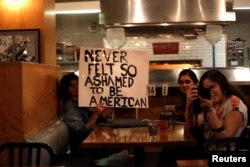 Patrons hold a sign as people march by while protesting the election of Republican Donald Trump as the president of the United States in downtown Los Angeles, California U.S., Nov. 9, 2016.