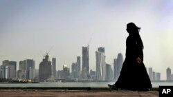 FILE- In this May 14, 2010 file photo, a Qatari woman walks in front of the city skyline in Doha, Qatar. 