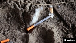 FILE - A discarded syringe is seen in the dirt with other debris under a highway overpass where drug users are known to congregate, in Everett, Washington, Feb. 16, 2017.