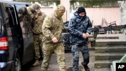 Seorang tentara Angkatan Laut Ukraina yang ditangkap (kanan), dikawal oleh petugas intelijen Rusia di Simferopol, Krimea, Selasa (27/11). 