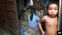 The child of a Cambodian prostitute stands in the doorway of a Phnom Penh slum shack as a group of sex workers play cards to pass the time, in this July 10, 2002 file photo.