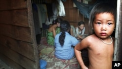 The child of a Cambodian prostitute stands in the doorway of a Phnom Penh slum shack as a group of sex workers play cards to pass the time, in this July 10, 2002, file photo.