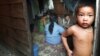 The child of a Cambodian prostitute stands in the doorway of a Phnom Penh slum shack as a group of sex workers play cards to pass the time, in this July 10, 2002 file photo.