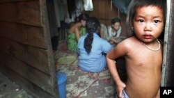 The child of a Cambodian prostitute stands in the doorway of a Phnom Penh slum shack as a group of sex workers play cards to pass the time, in this July 10, 2002 file photo.