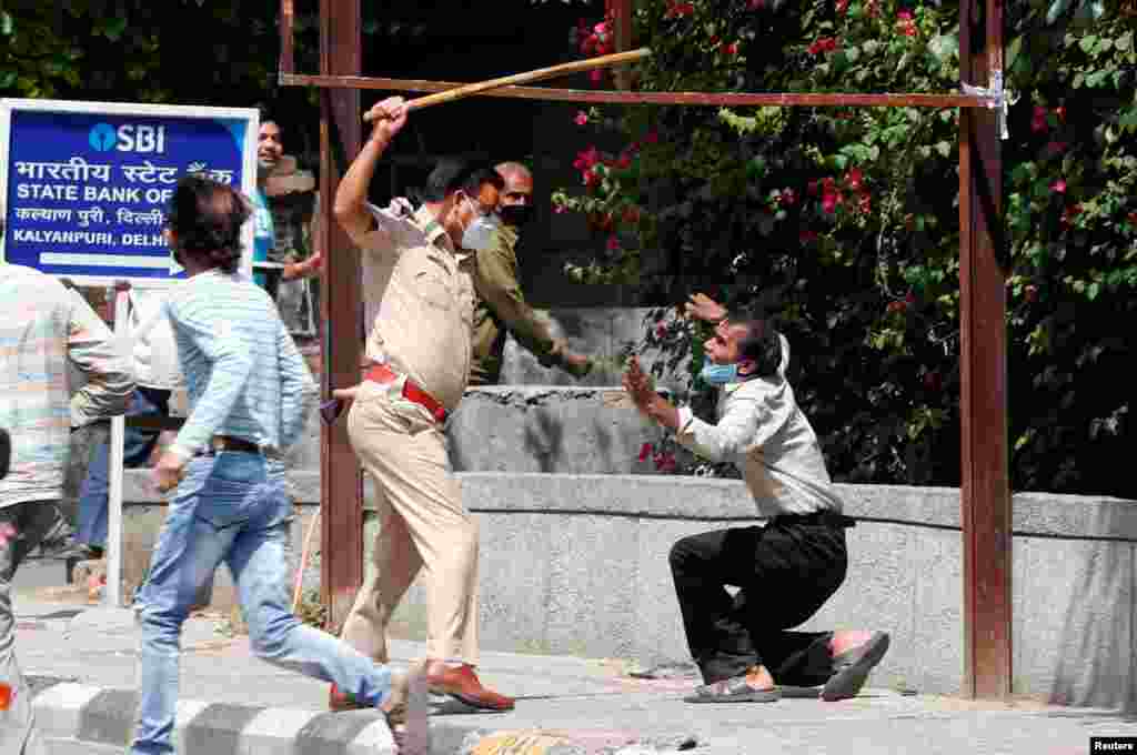 A police officer raises a baton at a man who, according to police, had broken the social distancing rule, outside a wine shop during an extended nationwide lockdown to slow the spread of the coronavirus disease (COVID-19), in New Delhi, India.