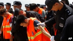 Chinese, in an orange vest, arrested over an alleged internet scam, are escorted by Chinese police officers before boarding at Phnom Penh International Airport, in Phnom Penh, Cambodia, Thursday, Oct. 12, 2017. Cambodia has deported dozens of Chinese cit