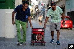 In this Oct. 20, 2017, photo, men push a generator along Fortaleza street, one month after Hurricane Maria hit San Juan, Puerto Rico.