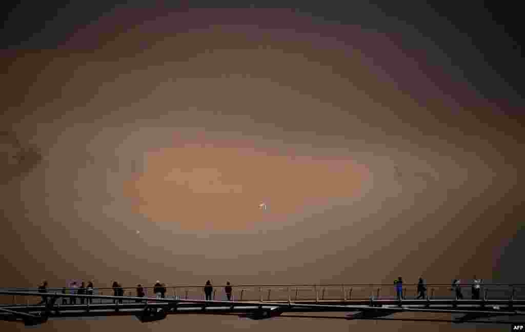 People cross the Millennium Footbridge with the sky darkened over London caused by warm air and dust from the storm Ophelia. The storm swept air and dust in from southern Europe. Social media users shared pictures of ominous-looking clouds blocking out the sun, prompting London&#39;s Science Museum to joke on Twitter: &quot;It&#39;s not the apocalypse!&quot;