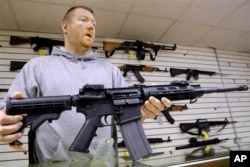 FILE - The owner of a gun shop holds one of the assault rifles his store sells.