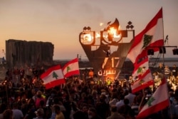 Anti-government protesters wave Lebanese national flags near a giant flame over a metal statue that reads in Arabic "October 17, Revolution," in Beirut, Lebanon, Oct. 17, 2020.