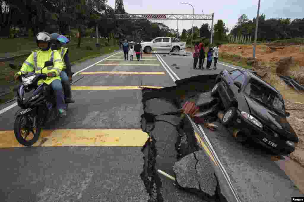 People ride past a road damaged by flooding at Kuala Krai in Kelantan, Malaysia. The worst flooding in Malaysia in more than a decade has killed 10 people and forced nearly 160,000 from their homes and more rain is expected, authorities said.