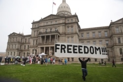 A protester carries a sign during a rally against Michigan’s coronavirus stay-at-home order at the State Capitol in Lansing, Mich., May 14, 2020.