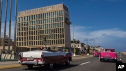 Para wisatawan mengendarai mobil klasik melintas gedung Kedubes AS di Havana, Kuba, 3 Oktober 2017.