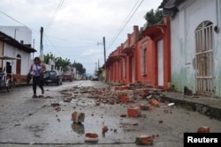 FILE - A woman walks past debris of a house damaged by an earthquake in Huixtla, in Chiapas state, Mexico, June 14, 2017.