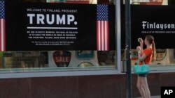 A woman takes a picture of a poster welcoming U.S. President Donald Trump and Russian President Vladimir Putin at a store in downtown Helsinki, July 14, 2018. Trump and Putin will meet Monday at Finnish presidential palace in Helsinki.