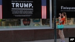 A woman takes a picture of a poster welcoming U.S. President Donald Trump and Russian President Vladimir Putin at a store in downtown Helsinki, July 14, 2018. Trump and Putin will meet Monday at Finnish presidential palace in Helsinki.