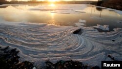 FILE - The sun rises above a polluted lake at the Nam Son garbage dump, north of Hanoi, Vietnam.