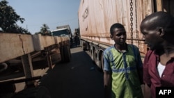 Deux hommes se tiennent au milieu d'un convoi de camions de marchandises bloqué sur la route nationale 1 en raison d'affrontements qui ont eu lieu 25 kilomètres plus loin sur la route entre des groupes armés et l'armée centrafricaine.