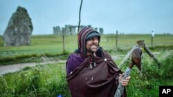 Un hombre posa delante del cerrado monumento de Stonehenge mientras personas se reúnen para celebrar el amanecer del día más largo en el hemisferio norte, el solsticio de verano, cerca de Salisbury, Inglaterra, el domingo 21 de junio de 2020.