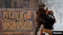 FILE - A police officer detains a demonstrator during a protest against Chile's government in Santiago, Chile, Nov. 5, 2019. The graffiti on the wall reads "Here they torture."