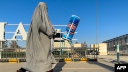 (FILE) An Afghan burqa-clad woman walks past an energy drink advertisement at Kandahar airport in Kandahar, on August 29, 2024.