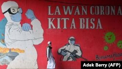 Seorang pria berjalan melintas mural tentang COVID-19 di Jakarta, 29 Januari 2021. (Foto: Adek Berry/AFP)