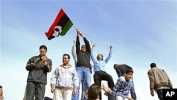Residents stand on a tank holding a pre-Gadhafi era national flag inside a security forces compound in Benghazi, Libya, February 21, 2011