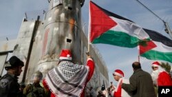 Warga Palestina, beberapa di antaranya mengenakan kostum Santa Claus berhadapan dengan polisi penjaga perbatasan Israel dalam aksi protes di Bethlehem, Tepi Barat Sabtu (23/12).