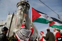 ປາ​ແລັສ​ໄຕ​ນ໌ ພາກັນແຕ່ງຕົວຊານຕາ ຄຣອດ (Santa Claus) ຫຼື ປາໆໂນແອລ ທີ່ປະເຊີນໜ້າກັບຕຳຫຼວດຊາຍແດນ ໃນຂະນະທີ່ມີການປະທ້ວງ ໃນເມືອງແວສ ເເບັຄ (West Bank) ຂອງເມືອງ ເບັຕເຕີແຮມ (Bethlehem), 23 ທັນວາ 2017.