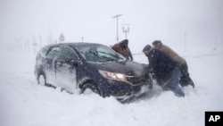 Beberapa orang membantu mendorong mobil yang terjebak salju tebal di Asbury Park, New Jersey, Kamis (4/1). 