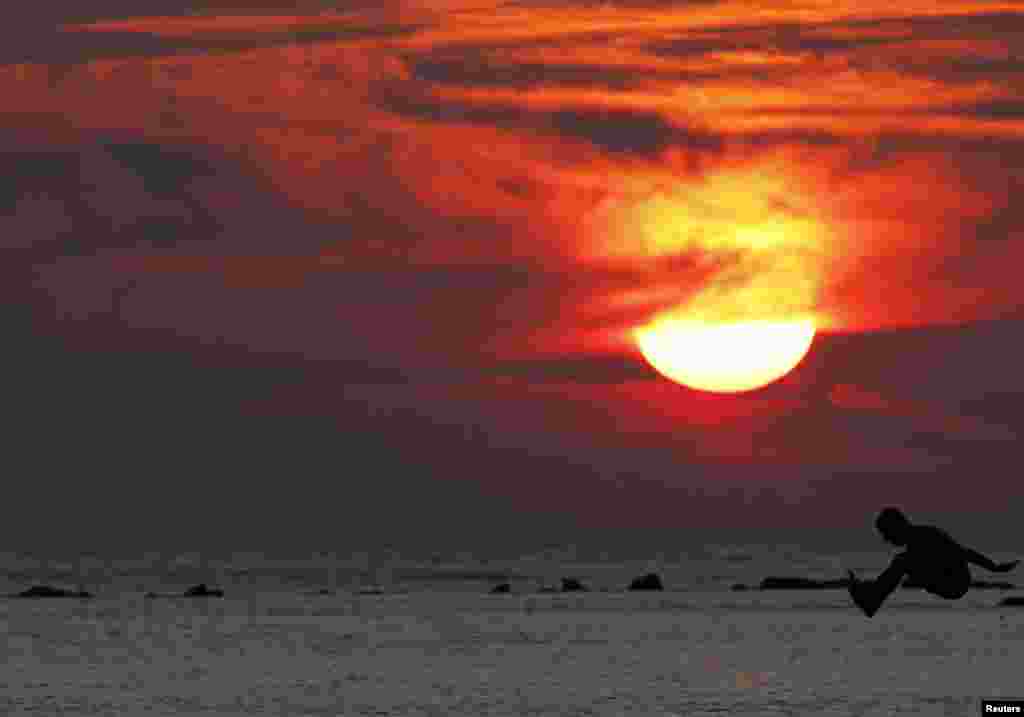 A boy is silhouetted as he jumps into the sea at a beach in the city of Durres, some 40 km (25 miles) from Tirana, Albania, Aug. 13, 2013.