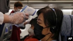 Stewardesses take temperatures of passengers as a preventive measure for the coronavirus on an Air China flight from Melbourne to Beijing before it land at Beijing Capital International Airport in China, Tuesday, Feb. 4, 2020. (AP Photo/Andy Wong)