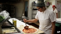 Andrea Ledesma spreads sauce on pizza dough at Classic Slice restaurant in Milwaukee. The 28-year-old has a four-year degree and quit a higher paying job because it made her miserable. Ledesma thought she would be making more at this point in her life and she's not alone.