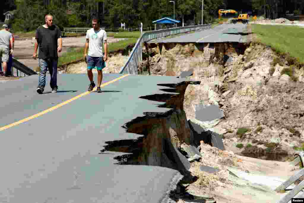 Local residents walk along the edge of a collapsed road that ran atop Patricia Lake&#39;s dam in the aftermath of Hurricane Florence, in Boiling Spring Lakes, North Carolina, Sept. 19, 2018.