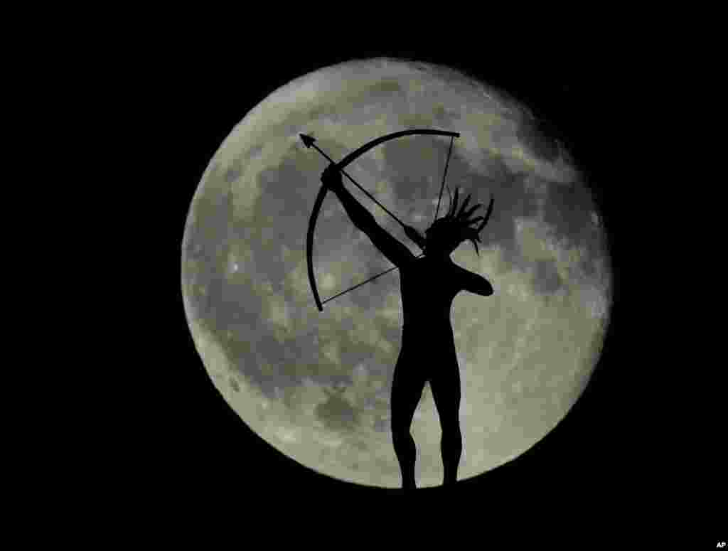 A waning full moon rises behind a statue of a Kansa Indian on top of the Kansas Statehouse, Sept. 17, 2016, in Topeka, Kansas, USA.