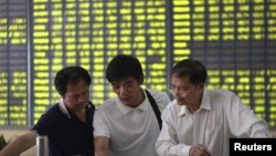 Investors talk in front of an electronic board showing stock information, filled with green figures indicating falling prices, at a brokerage house in Nantong, Jiangsu province, China, July 3, 2015. 