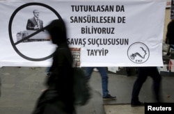 FILE - A woman walks past a banner picturing Turkish President Recep Tayyip Erdogan that reads, "When you arrest (journalists) or censor (media) we know that you are a war criminal, Tayyip," during a protest over the arrest of journalists Can Dundar and Erdem Gul in Ankara, Turkey, November 27, 2015.