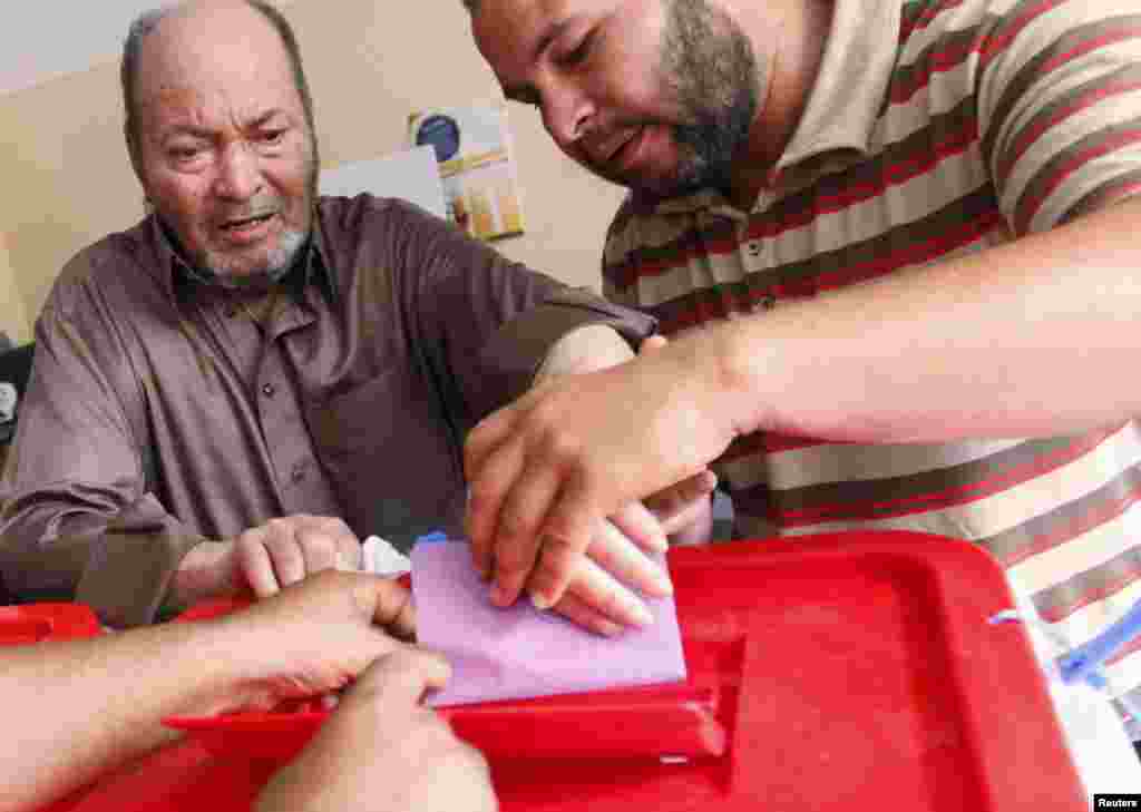 People help a voter place his ballot paper into the box at a polling station inside a school in Tripoli, June 25, 2014. 