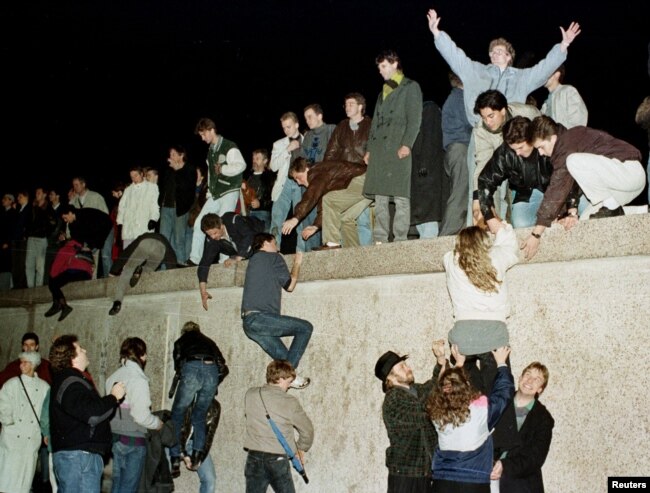 FILE - East German citizens climb the Berlin wall at the Brandenburg Gate as they celebrate the opening of the East German border in this November 10, 1989 file photo.