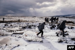 FILE - Migrants and refugees use their sleeping blankets to keep warm as they walk along snow covered fields after crossing the Macedonian border into Serbia, near the village of Miratovac, Jan. 18, 2016.