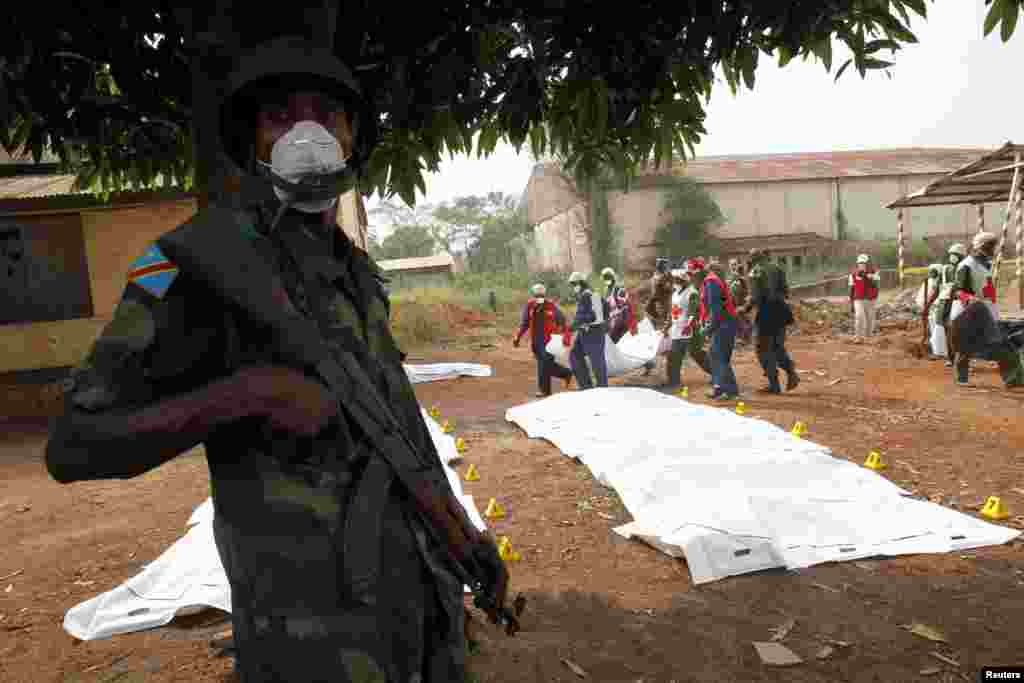 An African peacekeeping soldier stands guard as Red Cross workers move bodies from a mass grave at a military camp in Bangui, Feb. 17, 2014. 