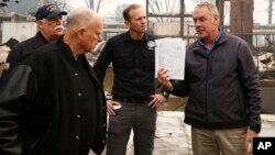 California Gov. Jerry Brown, second from left, looks at a students work book displayed by Interior Secretary Ryan Zinke, that was found during a tour of the fire ravaged Paradise Elementary School, Nov. 14, 2018, in Paradise, Calif.