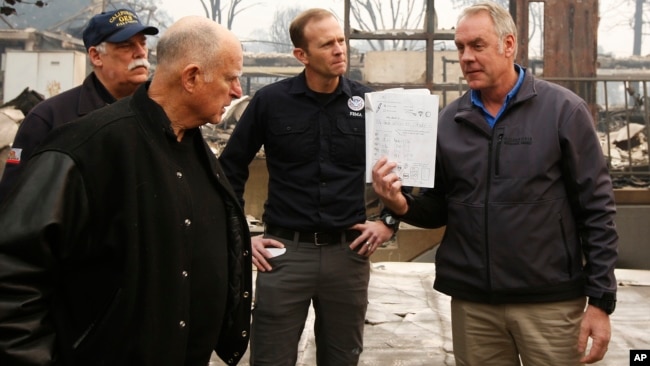 California Gov. Jerry Brown, second from left, looks at a students work book displayed by Interior Secretary Ryan Zinke, that was found during a tour of the fire ravaged Paradise Elementary School, Nov. 14, 2018, in Paradise, Calif.