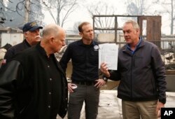California Gov. Jerry Brown, second from left, looks at a students work book displayed by Interior Secretary Ryan Zinke, that was found during a tour of the fire ravaged Paradise Elementary School, Nov. 14, 2018, in Paradise, Calif. The school is among the thousands of homes and businesses destroyed along with dozens of lives lost when the fire burned through the area last week.