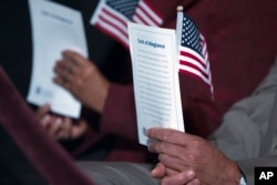 FILE - Participants hold the "Oath of Allegiance" and American flags during a naturalization ceremony at the National Archives in Washington, Dec. 15, 2015.