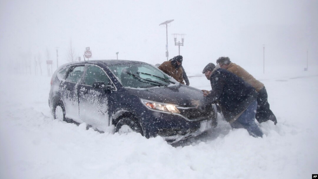Beberapa orang membantu mendorong mobil yang terjebak salju tebal di Asbury Park, New Jersey, Kamis (4/1). 