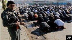 Un policier monte la garde tandis que des hommes prient à l'occasion de la Grande Fête, à Kaboul, Afghanistan
